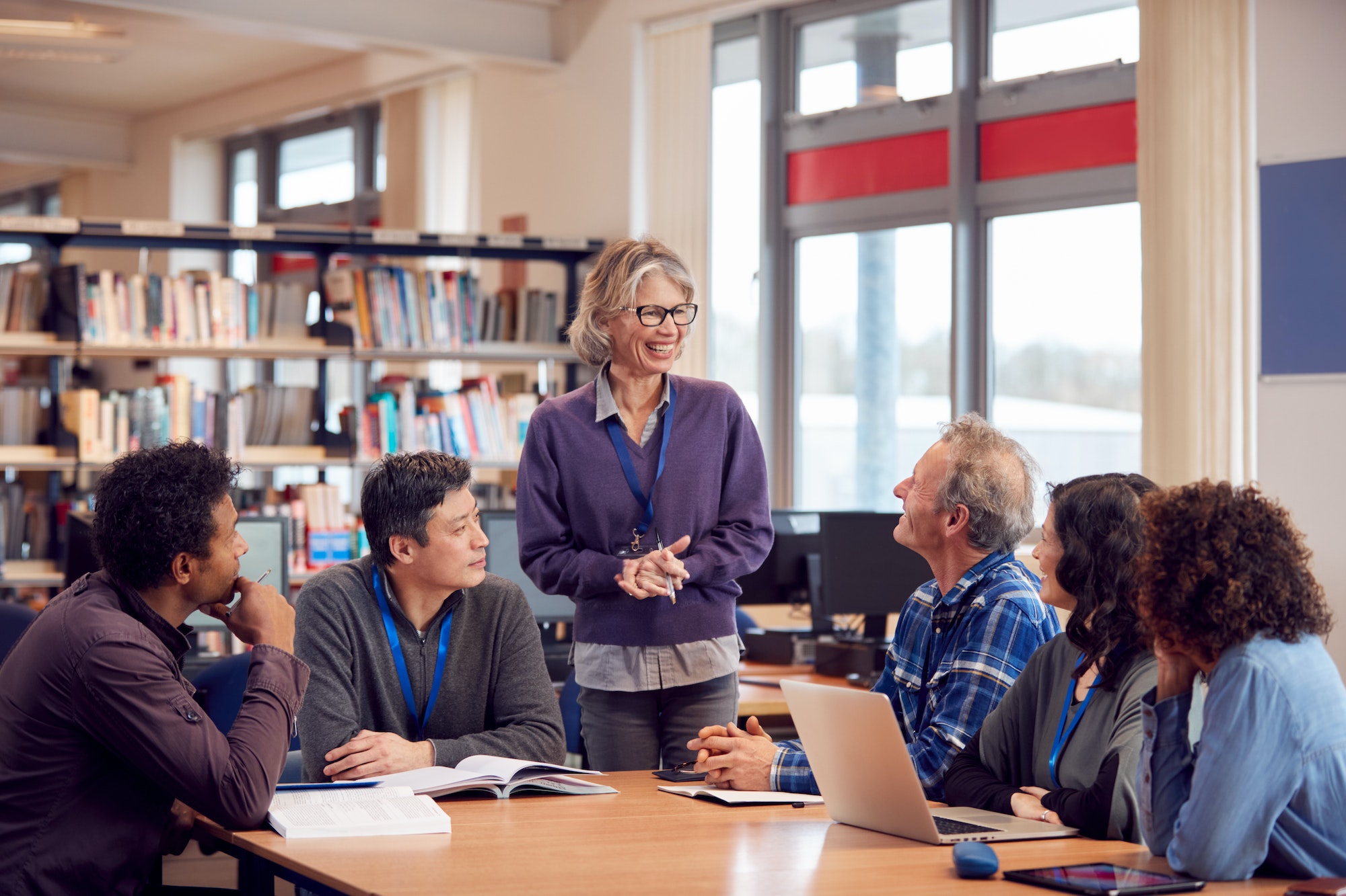 Teacher With Group Of Mature Adult Students In Class Sit Around Table And Work In College Library